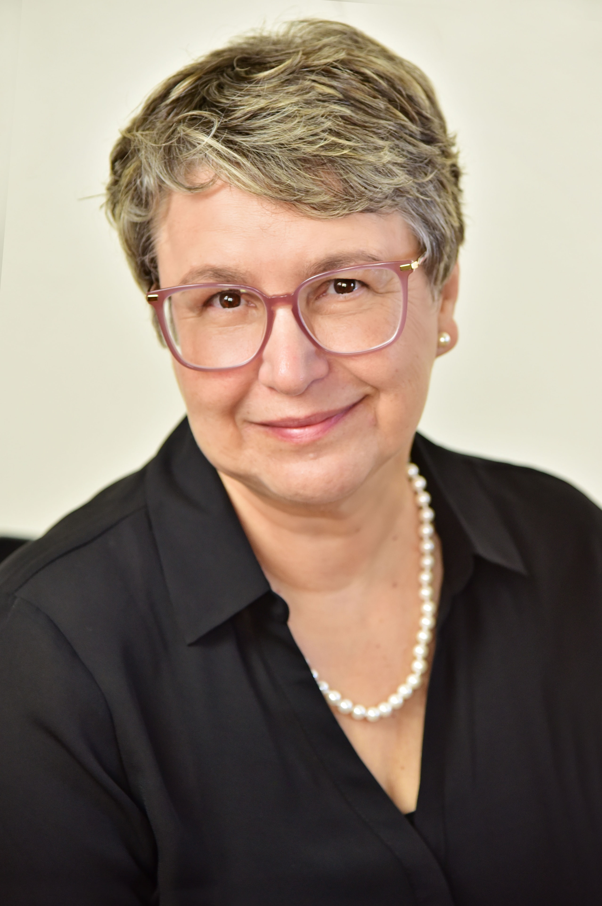 Professional woman with short gray hair and glasses smiling.